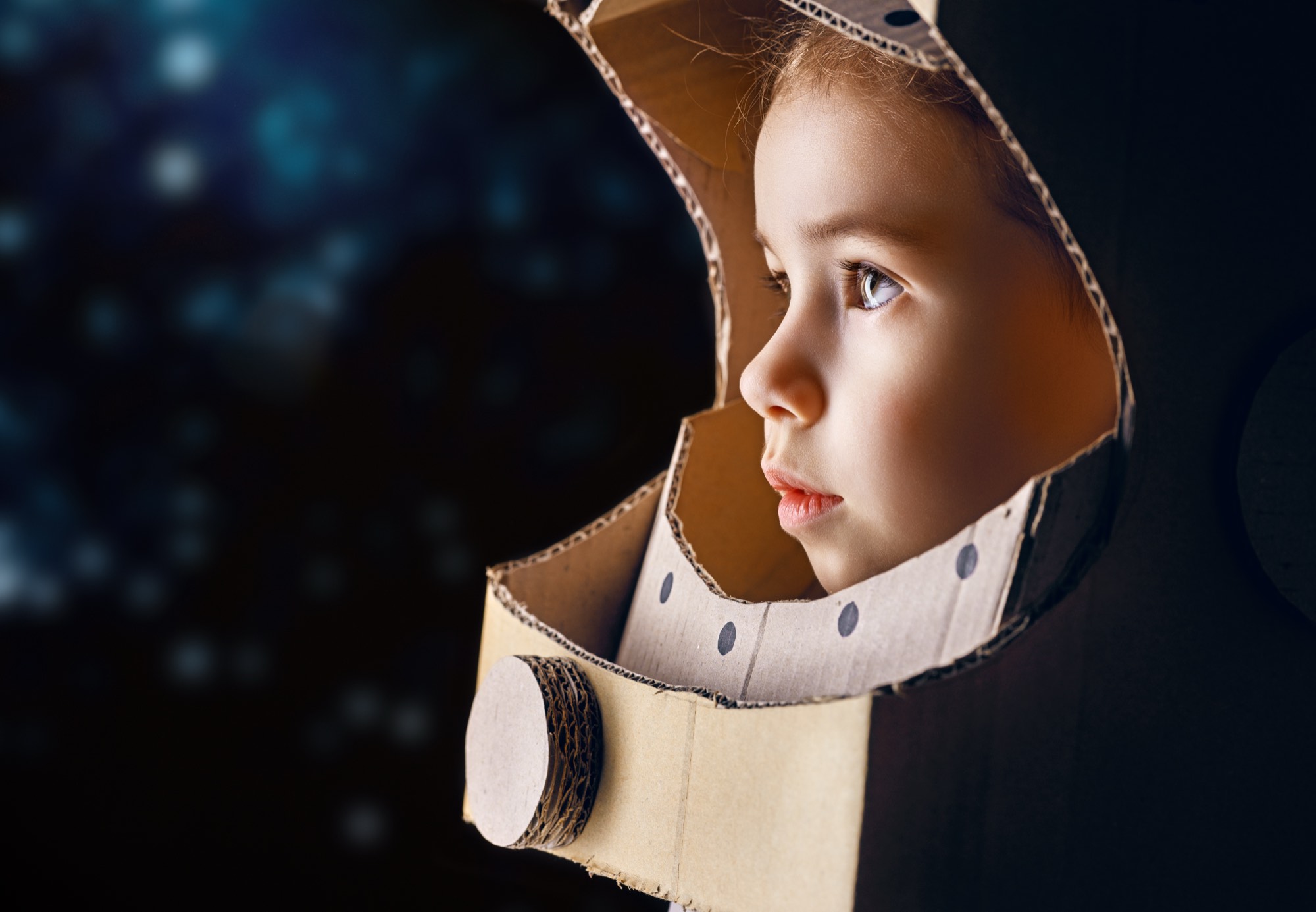 Kind mit selbstgebautem Astronautenhelm aus Karton blickt in den Sternenhimmel